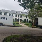 A house with moving trailer and truck in front of it.